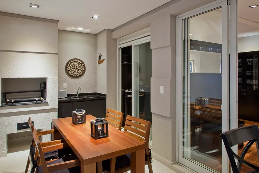 Varanda gourmet com churrasqueira e mesa de madeira rústica
