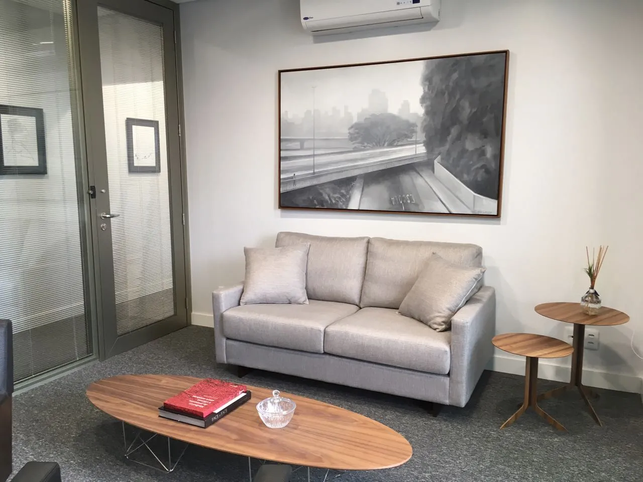 Lounge de escritório com sofá cinza e quadro urbano