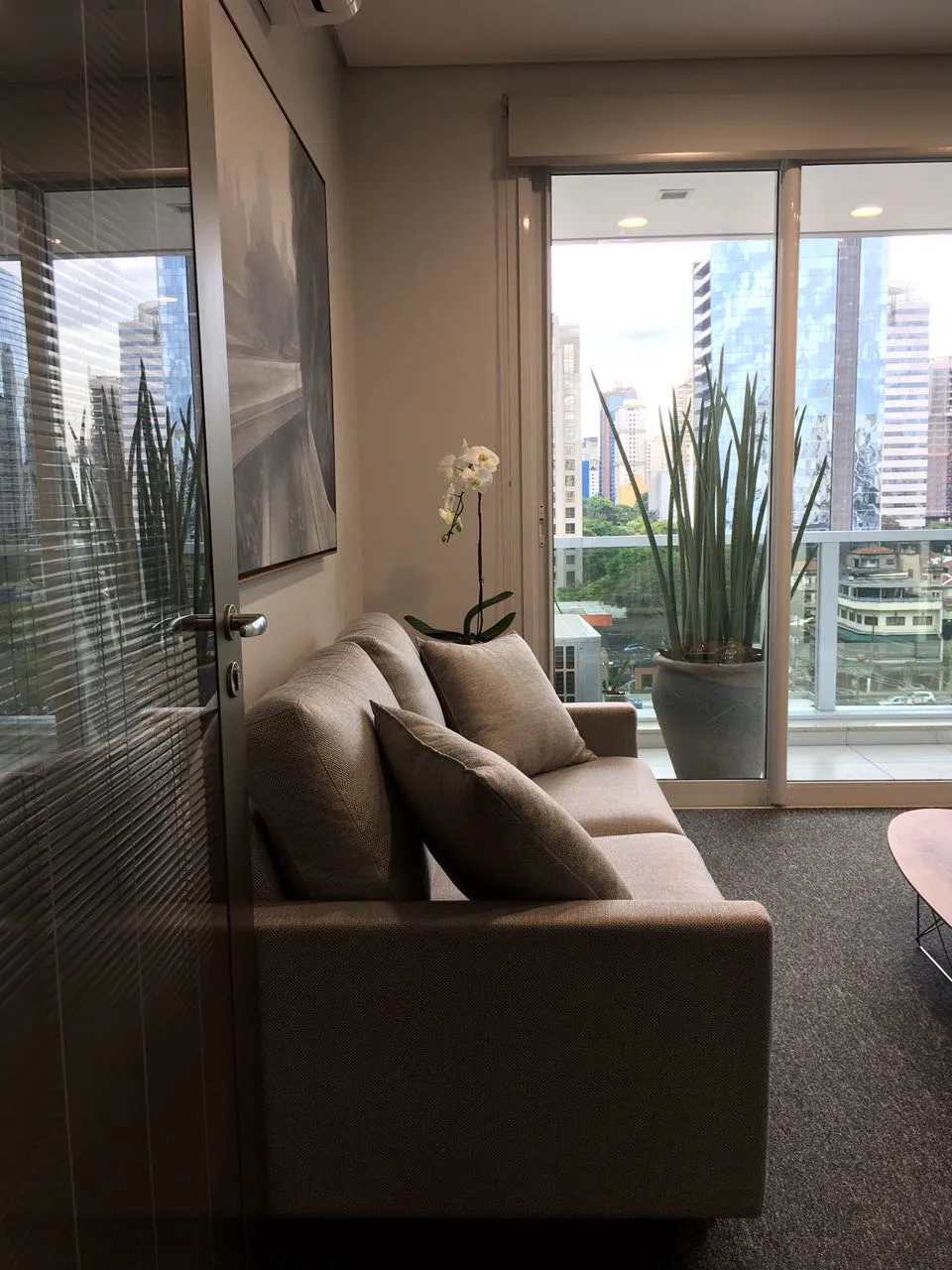 Sofá junto à varanda com vista urbana em escritório