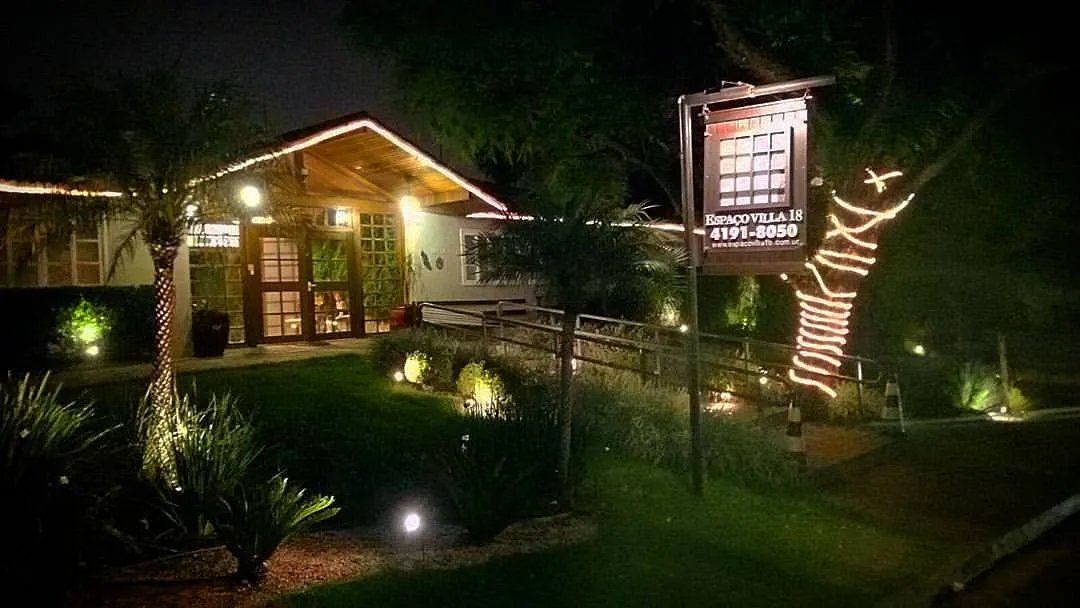 Placa iluminada do Espaço Villa 18 em jardim noturno